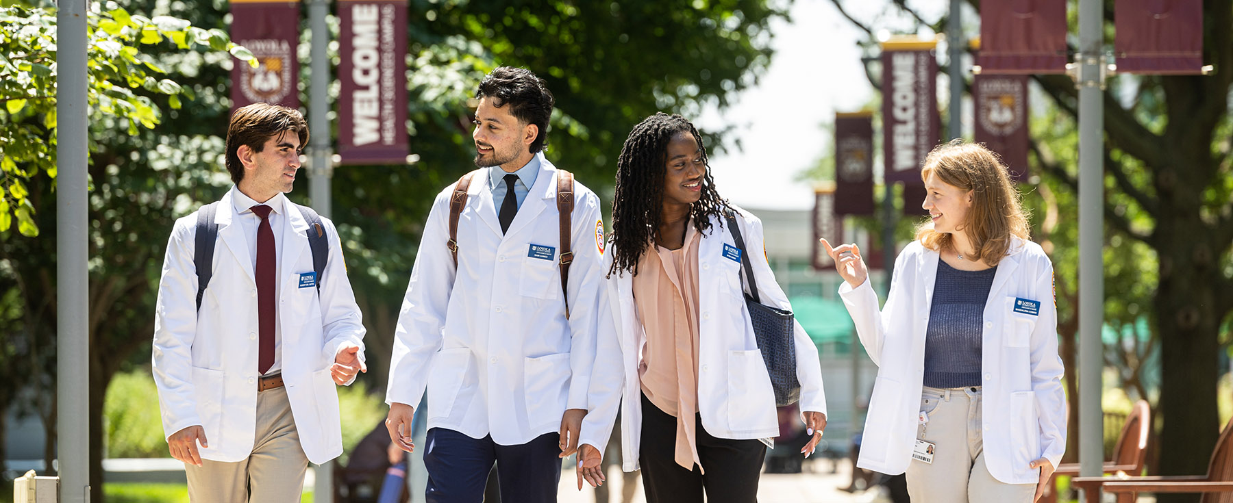 Four medical students wearing white coats walking and talking on campus